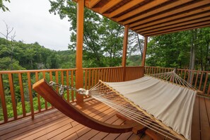 A hammock on a wooden deck with a view of a forested area.
