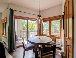 A round wooden table with chairs, a hanging pendant light, and a view of a balcony with a railing. - Corner Unit w/Pool | Walk to Village/Gondola (Keystone)