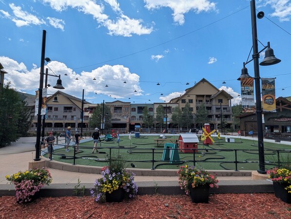 A plaza with a central lawn, surrounding buildings, and a few potted plants.