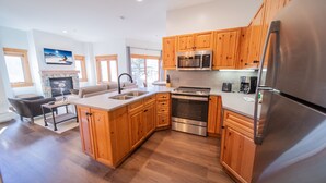 A modern kitchen with wooden cabinets, stainless steel appliances, and a stone fireplace. - Corner Unit w/Pool | Walk to Village (Keystone)