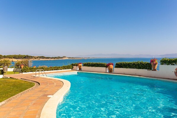 Relax by the serene pool overlooking the sea and distant mountains, surrounded by a beautifully maintained garden.