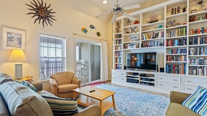 A living room with a sofa, armchair, coffee table, and a bookshelf filled with books. - FFR310 - Ocean Sky by First Flight Rentals (Kill Devil Hills, NC 27948)