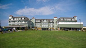 A large, multi-story building with a green facade and multiple windows. There is a parking lot in front with several cars parked. - FFR310 - Ocean Sky by First Flight Rentals (Kill Devil Hills, NC 27948)