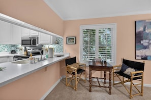 A kitchen with white cabinets, a microwave, a sink, and a dining area with a table and chairs.