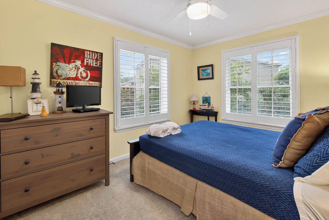 A bedroom with a bed, dresser, television, and windows.