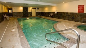 Una amplia piscina interior con suelo de baldosas y una zona de hidromasaje separada.