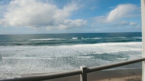 Vista a la playa con olas, cielo despejado y una barandilla.