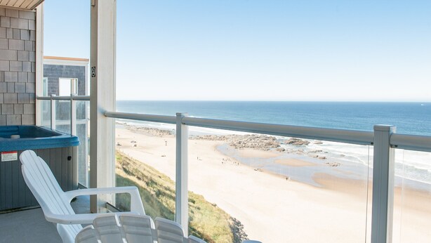 Un balcón con vistas a la playa, un jacuzzi y dos sillas blancas.