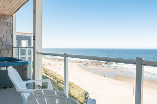 Un balcon avec vue sur la plage, un jacuzzi et deux chaises blanches.
