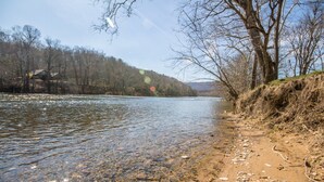A riverbank with clear water, pebbles, and leafless trees.