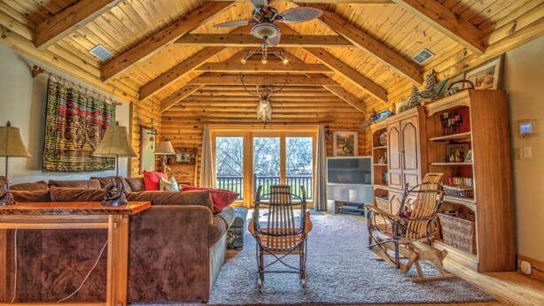 A spacious living room with a high wooden ceiling, a ceiling fan, a fireplace, a television, and a bookshelf.