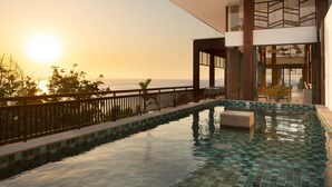 A modern outdoor swimming pool with a clear view of the ocean and sunset.