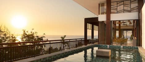 A modern outdoor swimming pool with a clear view of the ocean and sunset.