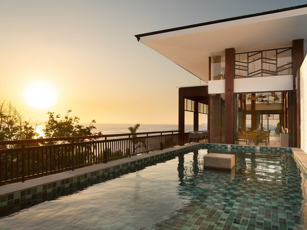 A modern outdoor swimming pool with a clear view of the ocean and sunset.