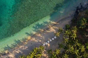 Vista aérea de uma praia com águas turquesa cristalinas, faixa de areia e uma fileira de guarda-sóis.