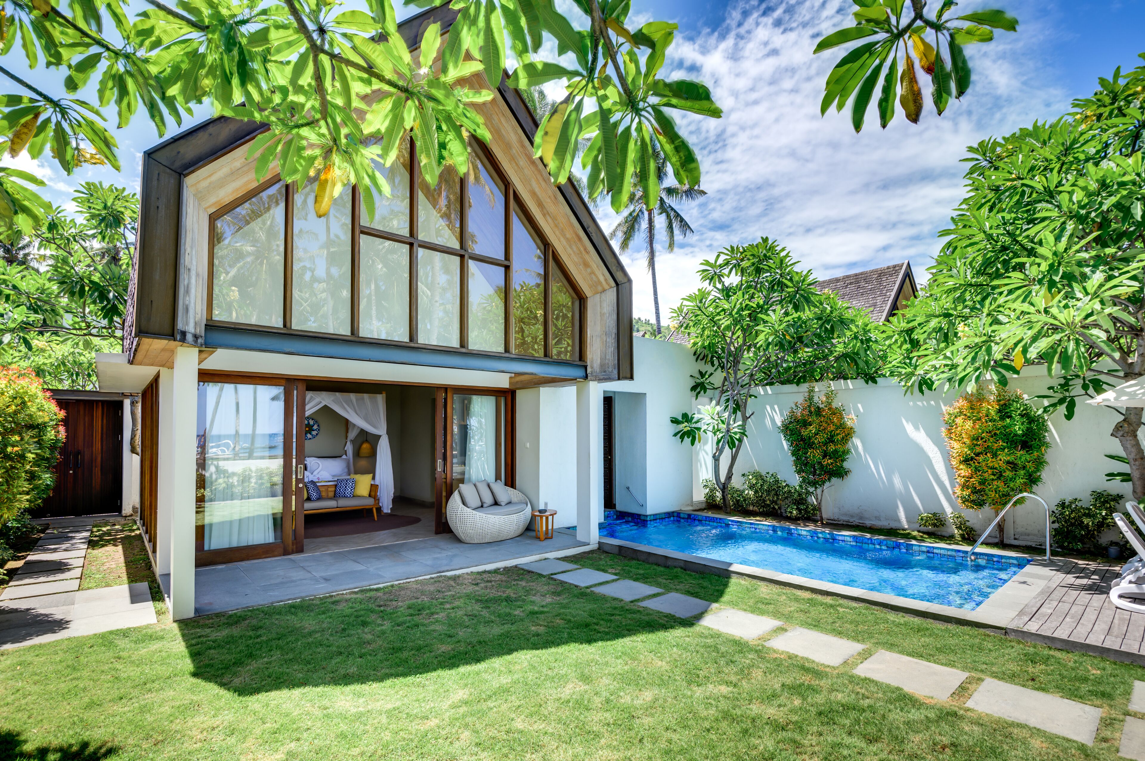 A modern house with a large glass window, a swimming pool, and a well-maintained garden.