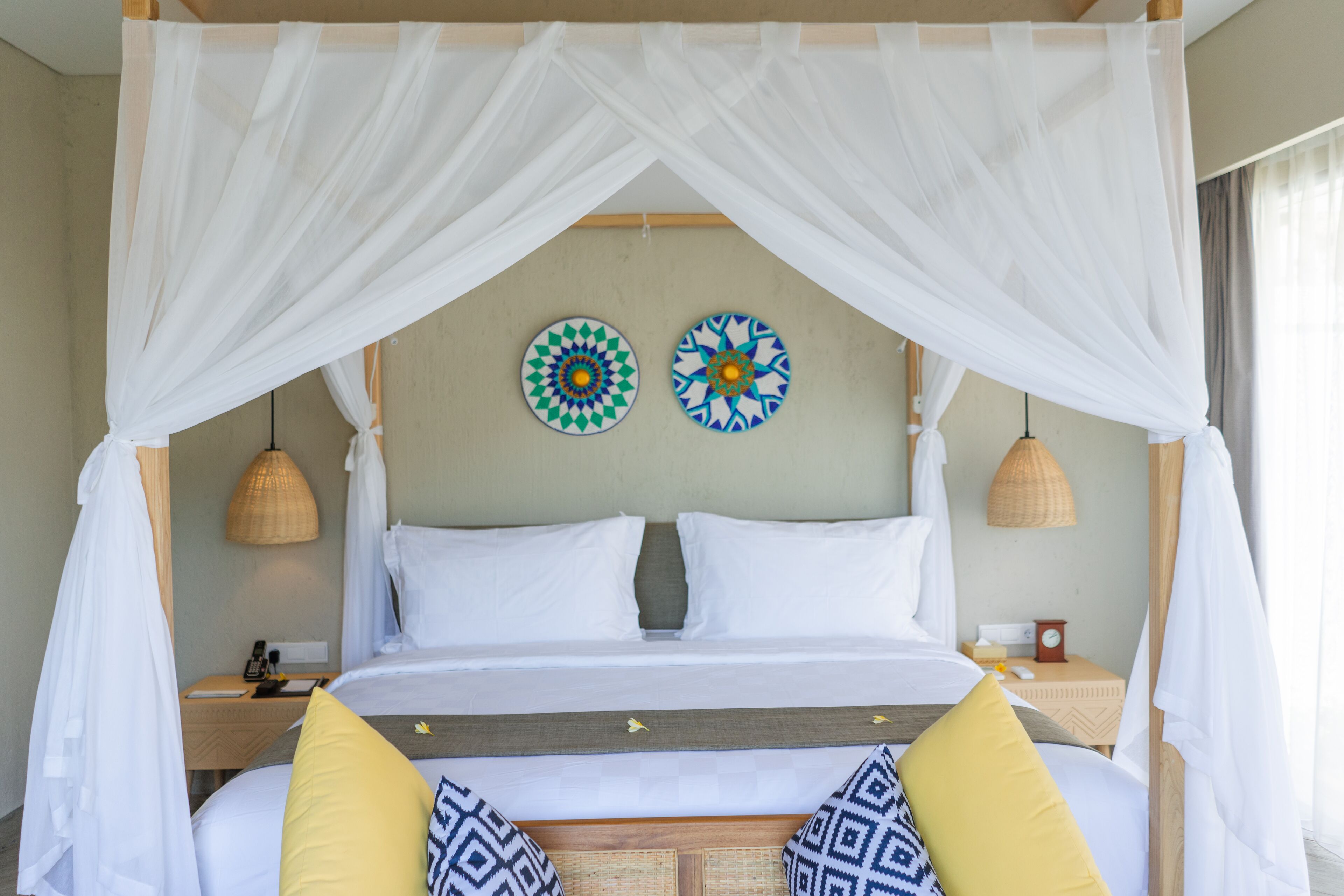 Una cama con ropa de cama blanca, un dosel y arte decorativo en la pared.