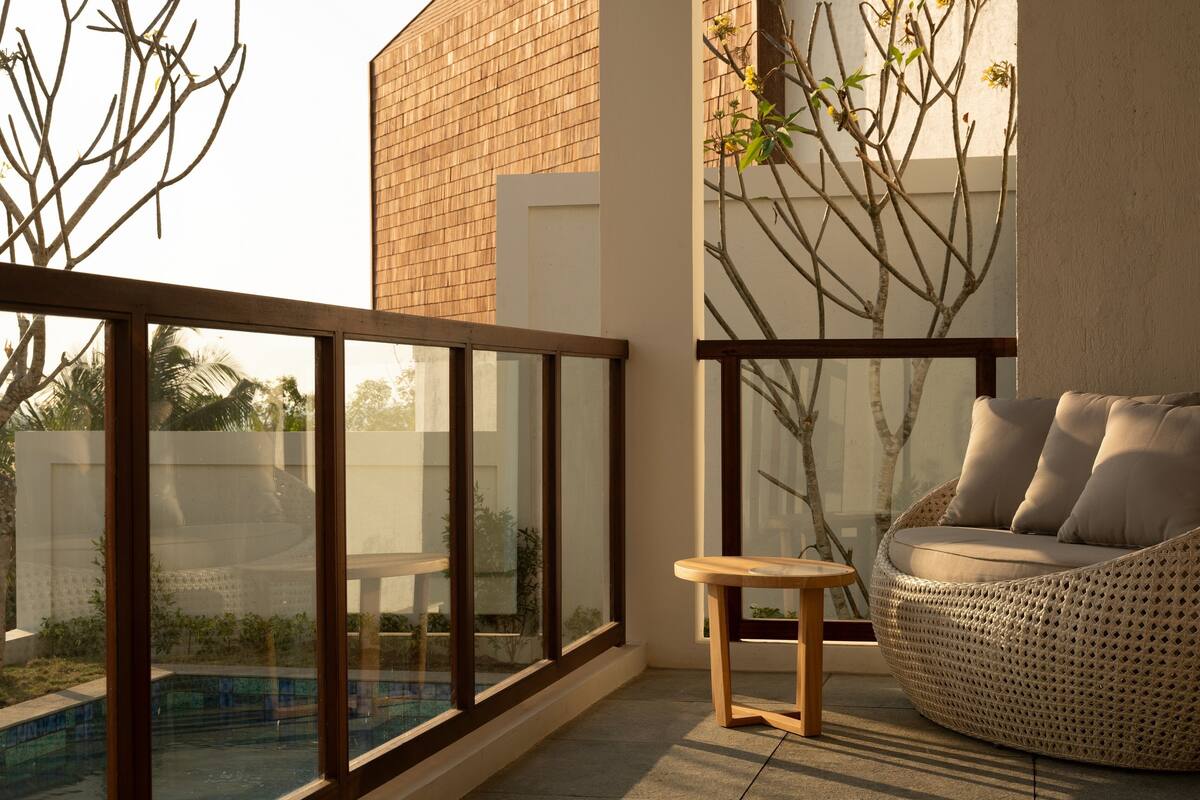 Een modern balkon met glazen hekwerk, een rieten bank en een klein houten tafeltje.