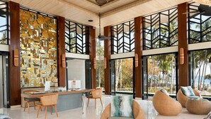 A spacious lobby with a modern design, featuring a reception desk, comfortable seating areas, and large windows offering views of palm trees and the ocean.