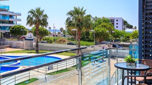 Ein Balkon mit Blick auf einen Swimmingpool, Palmen und moderne Gebäude.