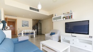 Ein modernes Wohnzimmer mit einer Couch, einem Fernseher, einer weißen Unterhaltungseinheit und einem Essbereich mit Stühlen und einem Tisch.