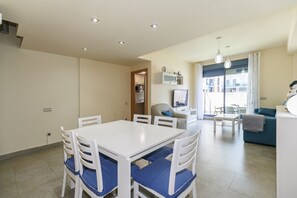 Uma sala de estar moderna com um sofá, uma mesa de jantar com cadeiras e uma cozinha ao fundo.