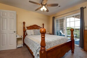 Un dormitorio con una cama de madera, un ventilador de techo, un puerta corrediza de vidrio a un balcón y una puerta blanca.