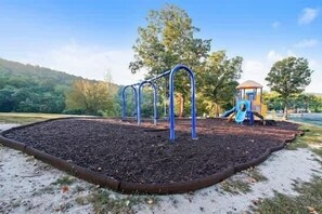 Un parque infantil con tobogán y estructuras para escalar, rodeado de árboles y cielo despejado.