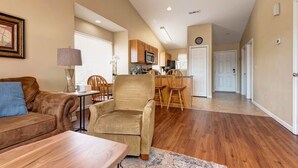 A living room with a sofa, armchair, and coffee table, a kitchen with wooden cabinets and appliances, and a hallway leading to a door. - 24-6 Serenity Escape Penthouse w/Indoor/Outdoor Pool / Splash Pad Near SDC (Branson)