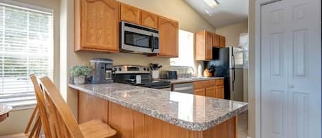 Cocina con armarios de madera, encimera de granito, microondas, estufa y refrigerador.