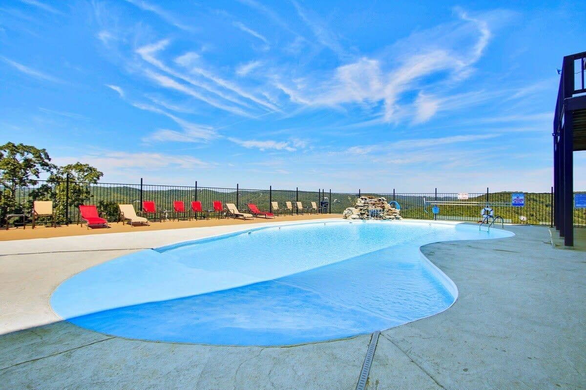 A swimming pool with a curved edge, surrounded by a fence. There are lounge chairs along the poolside.