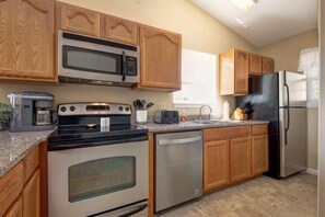 Una cocina con armarios de madera, un microondas de acero inoxidable, estufa, lavavajillas y refrigerador.