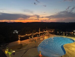 Ein Schwimmbad mit Blick auf den Sonnenuntergang, Liegestühle und Lichterketten.