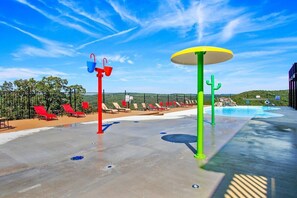 Un área de piscina con tumbonas rojas y verdes, una piscina pequeña y un cielo azul despejado.