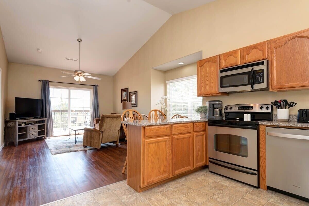 A kitchen with wooden cabinets, a microwave, stove, and a dining area with chairs.