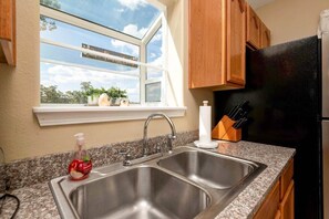 A kitchen with a double stainless steel sink, wooden cabinets, a black refrigerator, and a window with a view of the sky. - Serenity Escape Penthouse Heated Indoor Pool Splashpad (Branson)