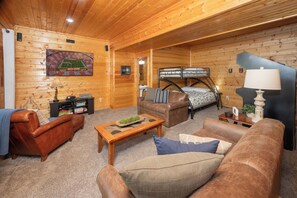 A wooden cabin interior with a living room, bunk beds, and a kitchen area.