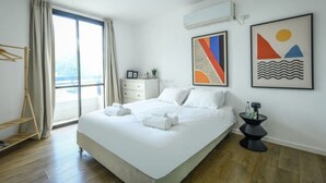 A modern hotel room with a large bed, a side table, a wardrobe, and a window with curtains. - Spacious 3BR Apartment Near Tel Aviv Beach (Tel Aviv)