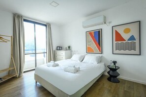 A modern hotel room with a large bed, a side table, a wardrobe, and a window with curtains.