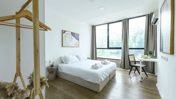 A modern bedroom with a large bed, a wooden hanger, a desk with a chair, and a window with curtains. - Spacious 3BR Apartment Near Tel Aviv Beach (Tel Aviv)
