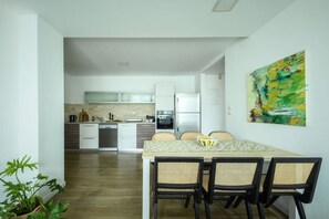 A modern kitchen with white cabinets, a dining table with four chairs, and a painting on the wall.