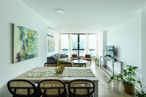 A modern living room with a dining area, large windows, and a flat-screen TV.