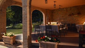 Un espace extérieur aménagé pour les repas, avec des arches en briques, des tables dressées et des plantes en pot.