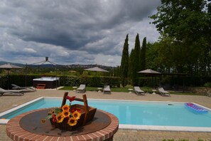Un espace piscine avec des chaises longues, un jacuzzi et une vue sur une ville lointaine.