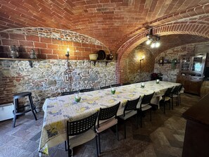 Une pièce aux murs de pierre, avec une longue table dressée pour le repas, des chaises et un petit tabouret.