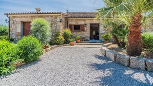 A stone house with a gravel driveway, potted plants, and a palm tree. - FRANCISCA  Ref. VP03 (Alcúdia)