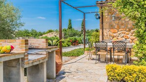 An outdoor patio with a barbecue grill, a table with chairs, and a stone wall with a lantern. - FRANCISCA  Ref. VP03 (Alcúdia)