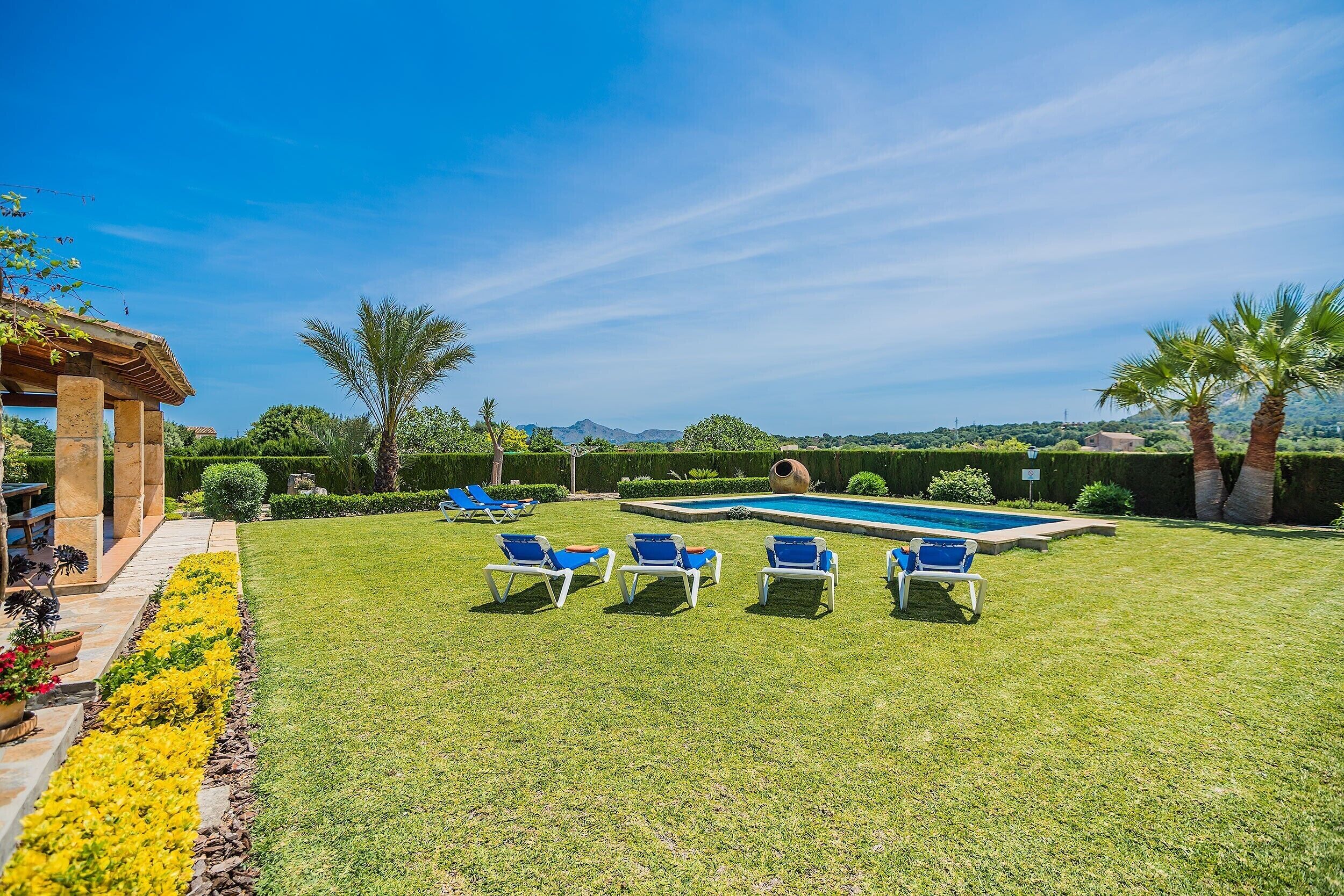 Ein gepflegter Rasen mit Swimmingpool, blauen Liegestühlen und einer Pergola.
