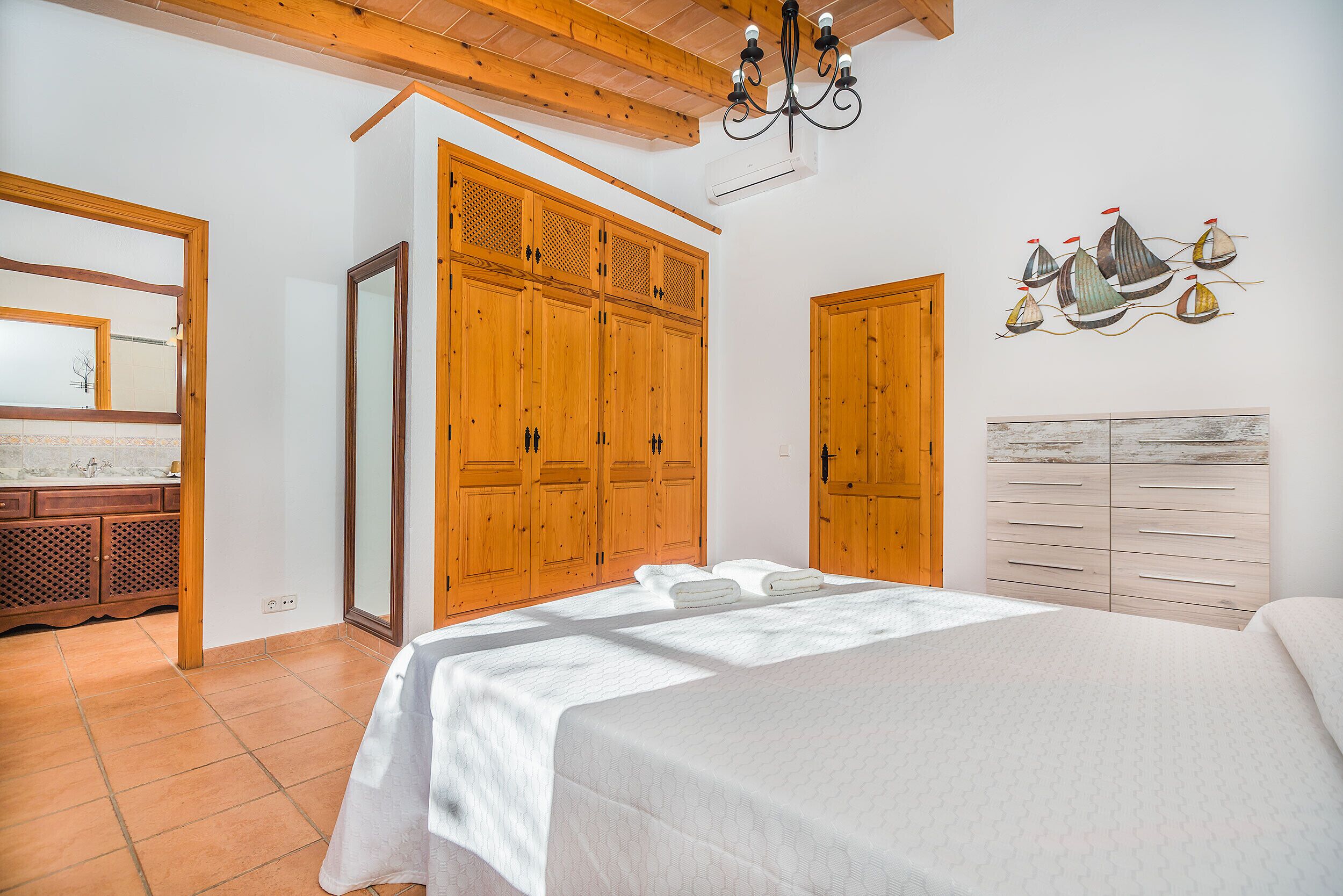 A bedroom with a large bed, wooden wardrobe, and a wall-mounted artwork of sailboats.