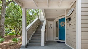 A covered porch with a set of concrete steps leading to a blue door with a wreath. - Ground Floor Cottage with Free Beach Service! (Miramar Beach)